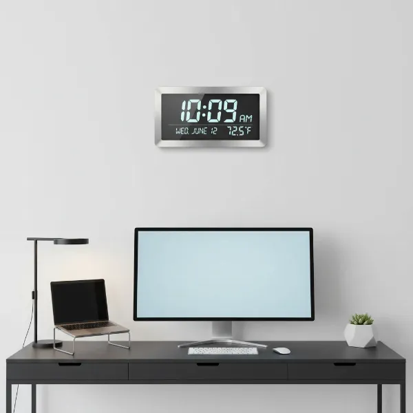 A modern digital wall clock showing time, date, and temperature, positioned above a sleek office desk.